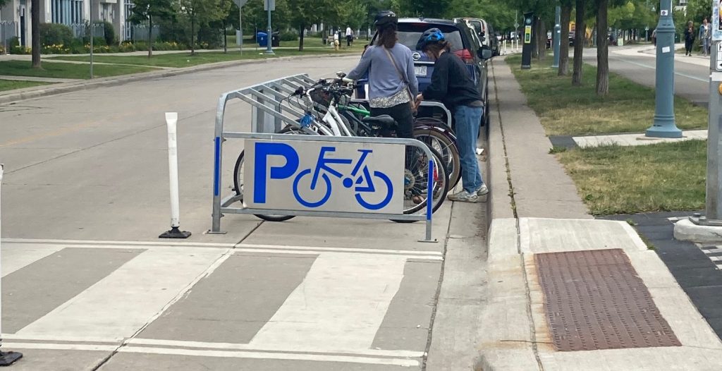 People park their bikes at a bike corral located on a street.