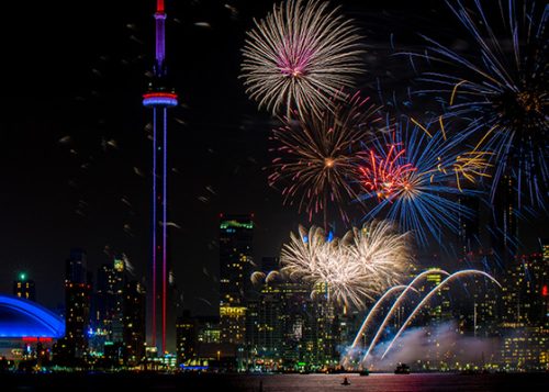 Fireworks over the Toronto downtown skyline with the CN Tower lit up in blue and red.