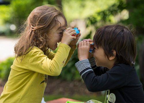 Two little children are smiling happily as they use a paper telescope to look at each other.