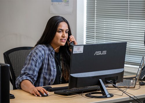 A woman talking a phone while working at a computer.