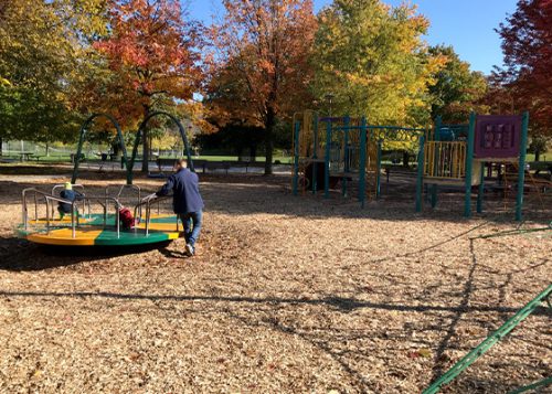 One adult and two children are playing at the playground in the park during the fall season.