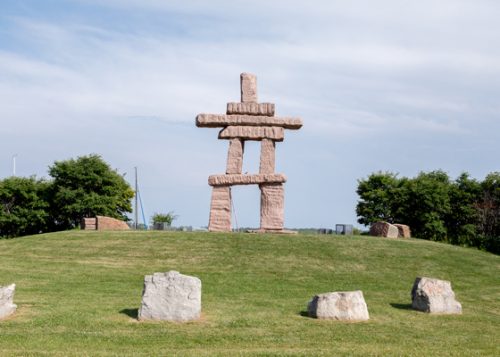 Inukshuk standing on top of a grassy hill surrounded by a ring of boulders
