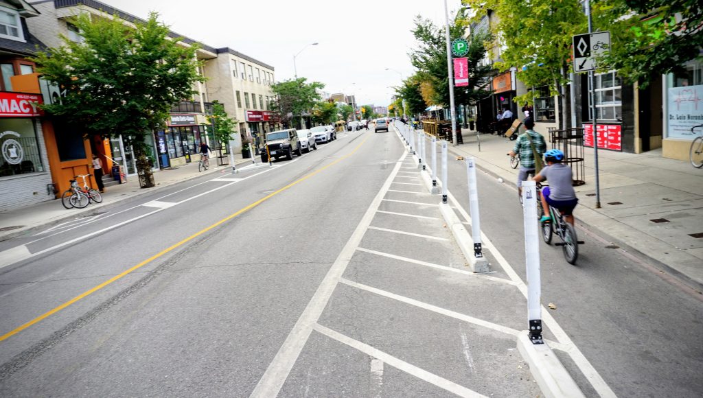 An adult and child cycle in a bike lane protected by concrete curbs and flex posts.