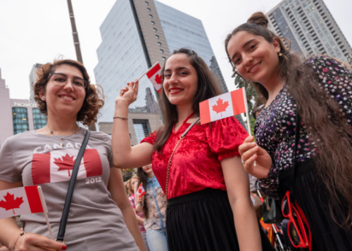 Three people dressed for Canada Day and holding Canadian flags.