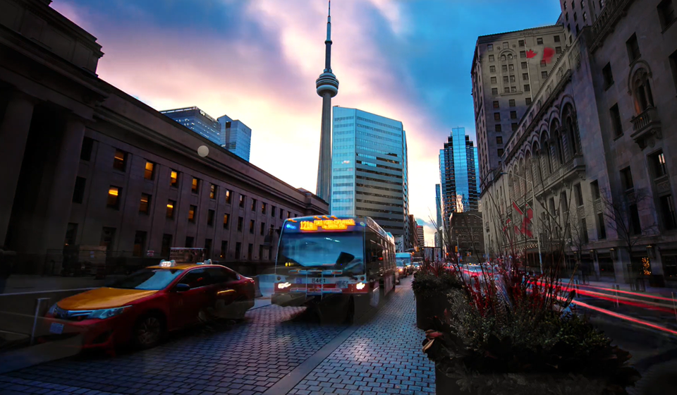 Bus and taxi driving on road with city buildings and CN tower in the background
